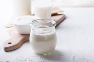 Unlabeled glass of yogurt in the foreground with a ceramic bowl of yogurt and a glass of milk in the background, highlighting UV decontamination of dairy products, packaging, surfaces, air and water.